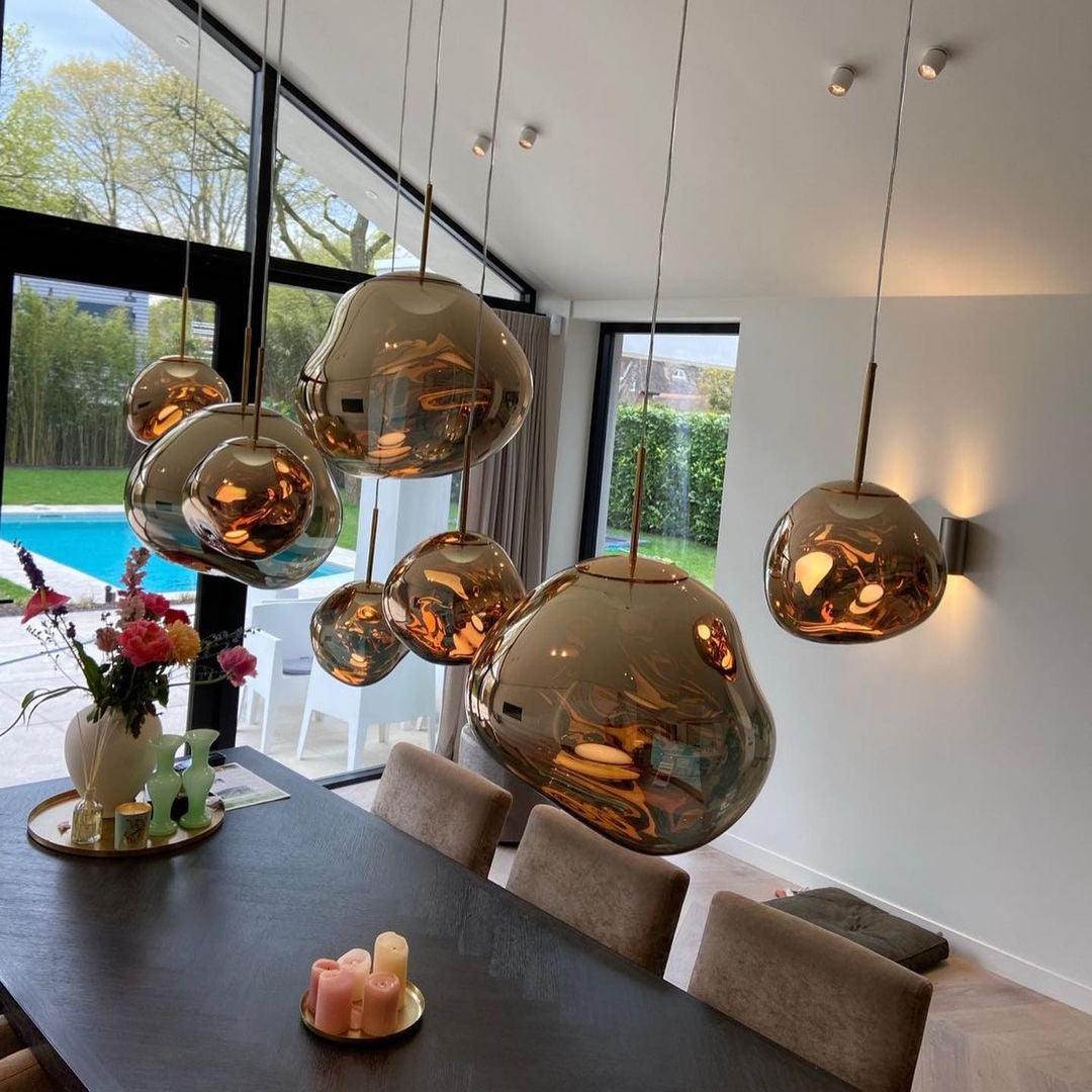 Gold molten pendants hung in a row above a dining table beside tall windows