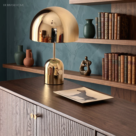 Gold dome table lamp on a fluted sideboard against a teal shelved wall