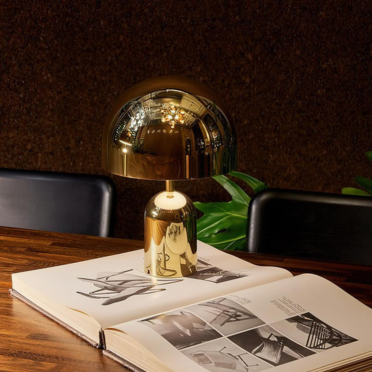 Gold dome lamp lit beside an open art book on a dark desk