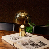 Gold dome lamp lit beside an open art book on a dark desk