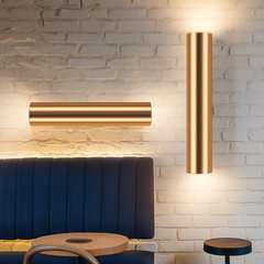 Gold tube sconces lit on a white brick wall above seating