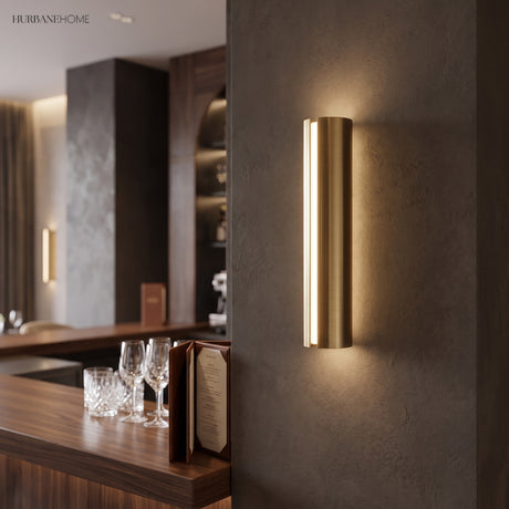 Gold tube sconce lit on a dark wall beside a timber cabinet