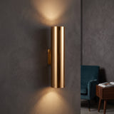 Gold tube sconce lighting a grey wall above and below