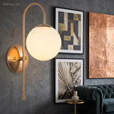 Gold arched sconce with a glowing globe beside framed artwork