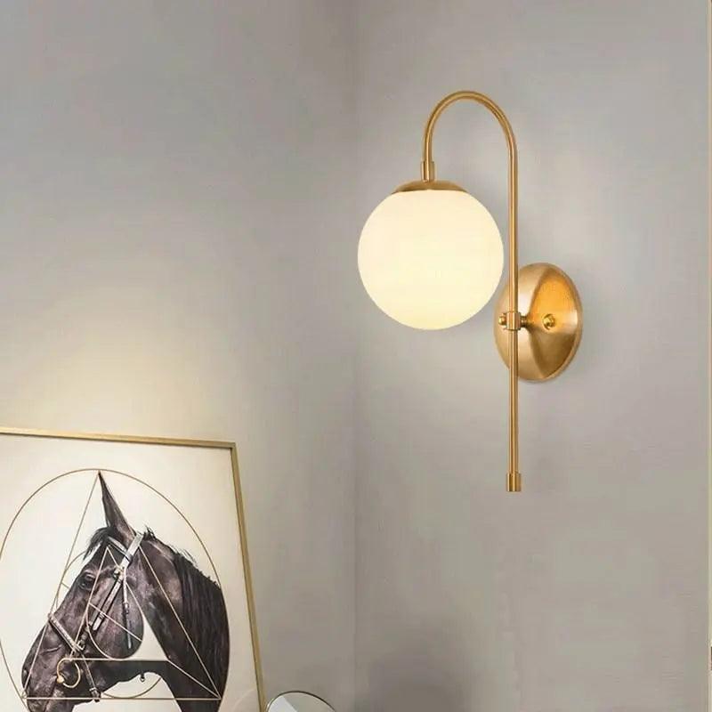 Gold globe sconce lit on a white wall above leaning pictures