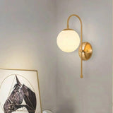 Gold globe sconce lit on a white wall above leaning pictures