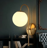 Gold arched arm wall sconce with a milk glass globe on a green wall