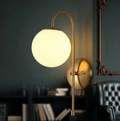 Gold arched arm wall sconce with a milk glass globe on a green wall