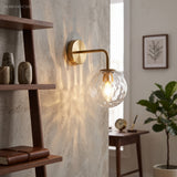 Gold globe sconce beside a leaning shelf and a potted fig tree