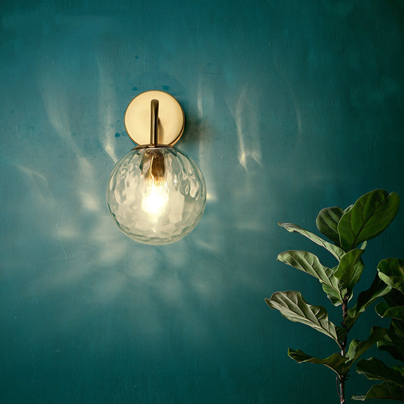 Rippled globe sconce lit against a deep teal wall beside a plant