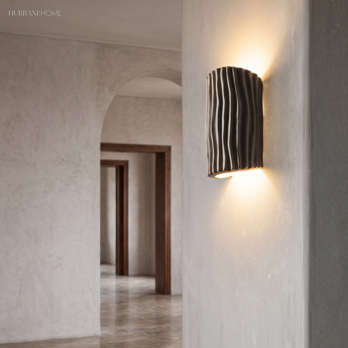 Gray textured wall sconce mounted on a plaster pillar by a hallway archway
