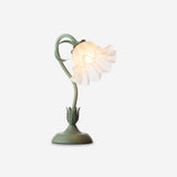 Green flower table lamp with lit white ruffled petal shade on a plain background