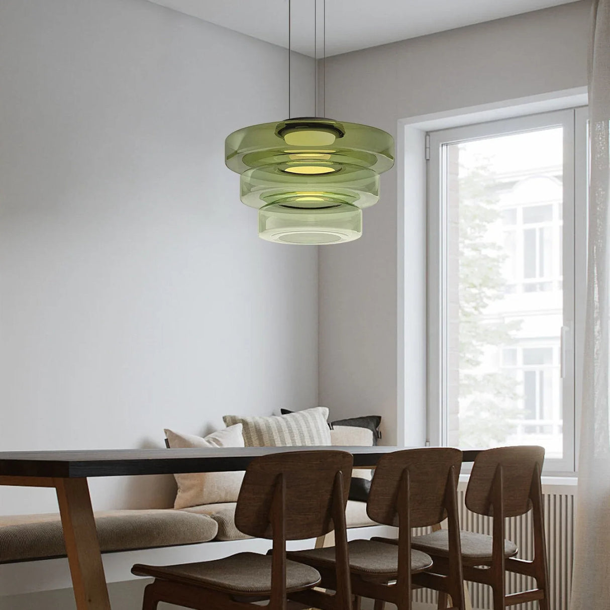 Green three-layer glass pendant light over a dark dining table by a window
