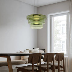Green three-layer glass pendant light over a dark dining table by a window