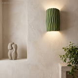 Green half cylinder wall sconce in a plaster niche near a stone sculpture
