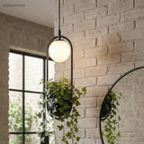 Planter pendant with a globe light hanging by a white brick wall