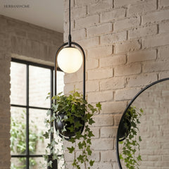 Planter pendant with a globe light hanging by a white brick wall