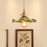 Green hibiscus glass pendant with a brass holder above a framed botanical print