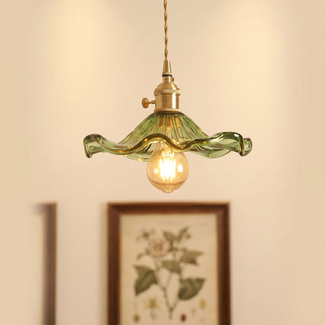 Green hibiscus glass pendant with a brass holder above a framed botanical print