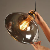 Hands holding the smoke glass dome shade around a lit Edison bulb