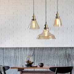 Three clear glass pendants above a dark marble counter and white brick wall