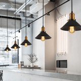 Row of black cone pendants lit along a concrete counter in a cafe