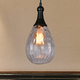 Clear teardrop pendant lit warm on an ochre wall above dark panelling