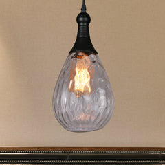 Clear teardrop pendant lit warm on an ochre wall above dark panelling