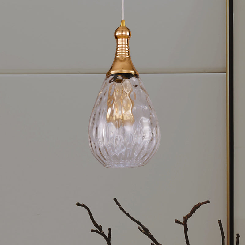 Clear teardrop pendant on a pale wall above a vase of bare branches