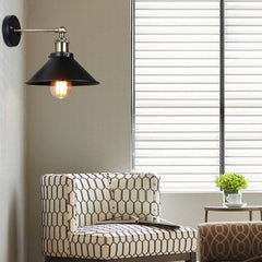 Black cone shade wall sconce lit on a green wall beside a window blind