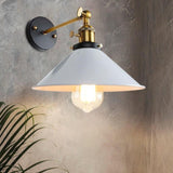 White cone shade wall sconce with a brass arm lit on a grey wall