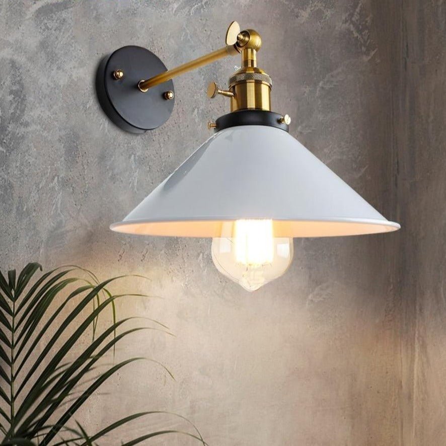 White cone shade wall sconce lit on a grey wall beside a palm plant