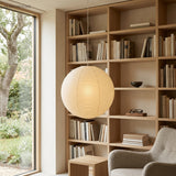 Paper globe pendant lighting a reading corner beside tall oak bookshelves