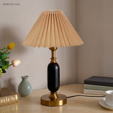 Khaki pleated shade lamp with black column and brass foot on a desk