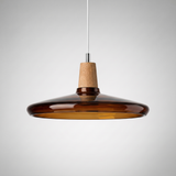 Wide amber glass saucer shade lit from within above a wood top