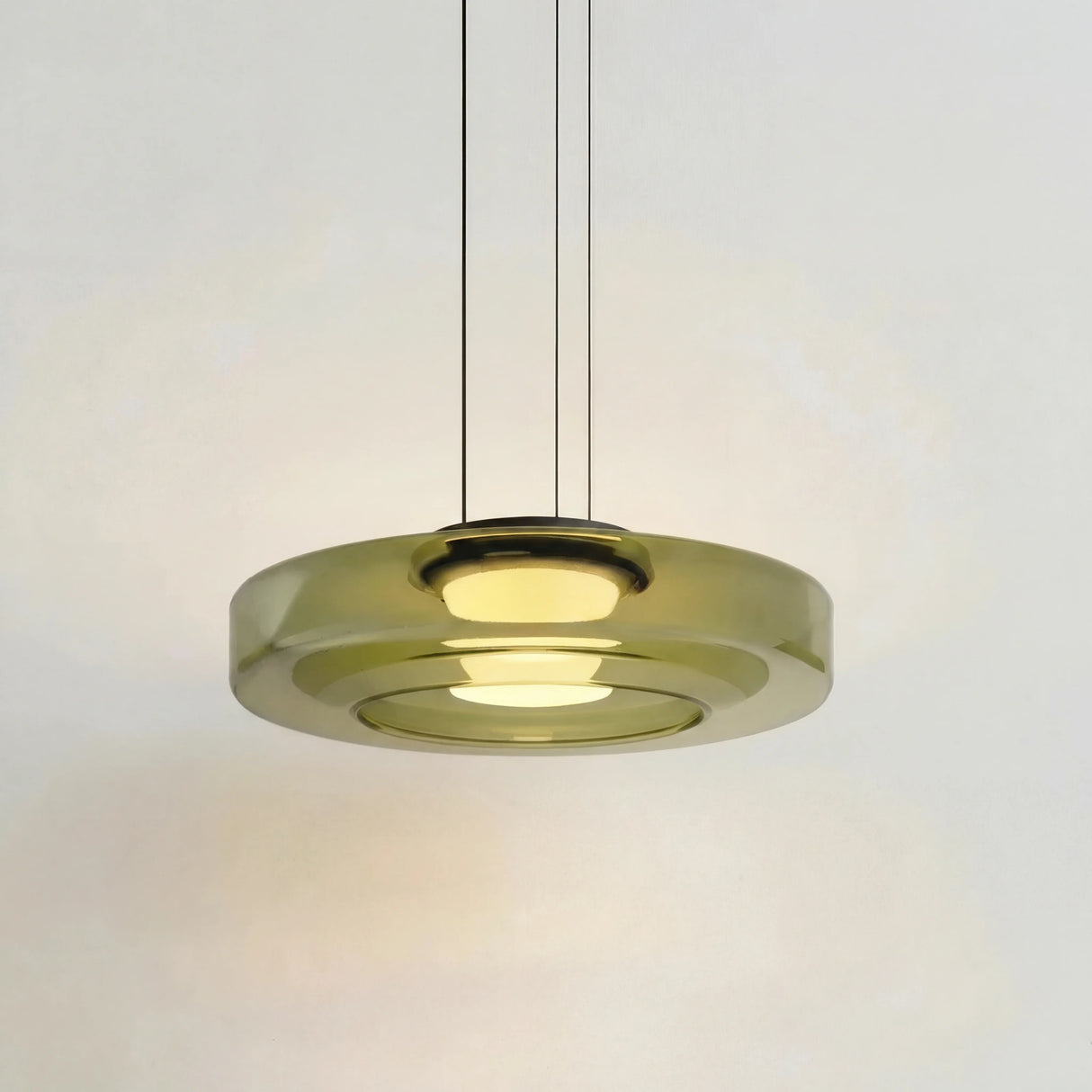 Green tinted glass disc pendant light glowing warmly on a studio background
