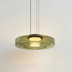 Green tinted glass disc pendant light glowing warmly on a studio background