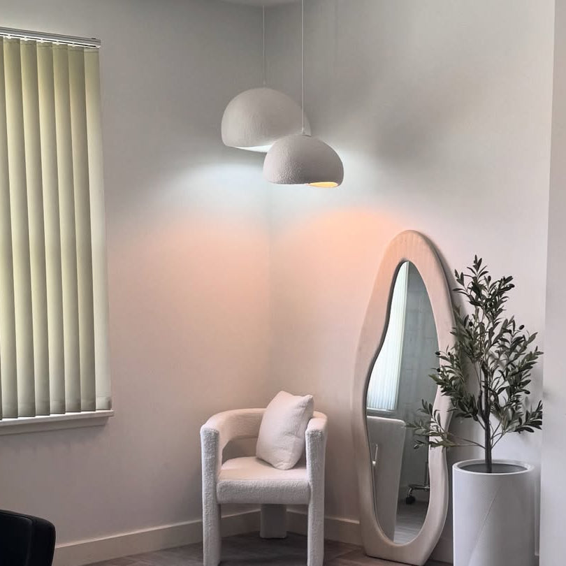 Two white dome pendants lit beside a tall mirror and plant