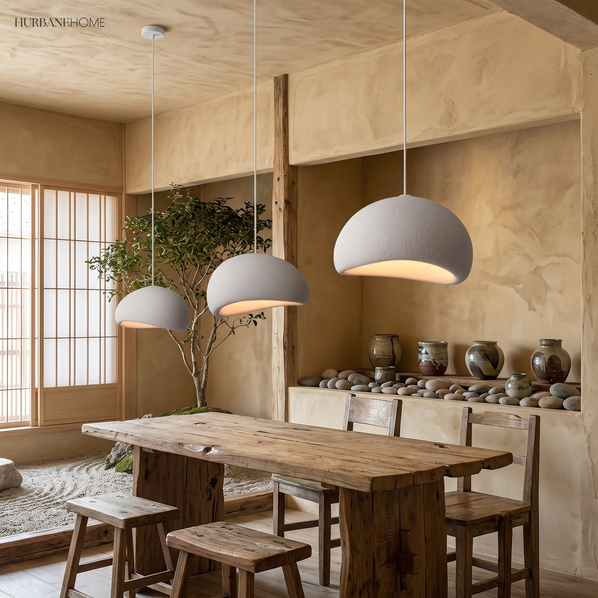 Three white wabi sabi pendants lit above a long dining table