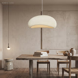 White wabi sabi pendant lit above a long table in a plaster room