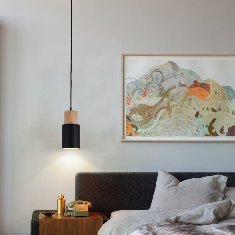 Black cylinder pendant hanging beside a bed as a reading light