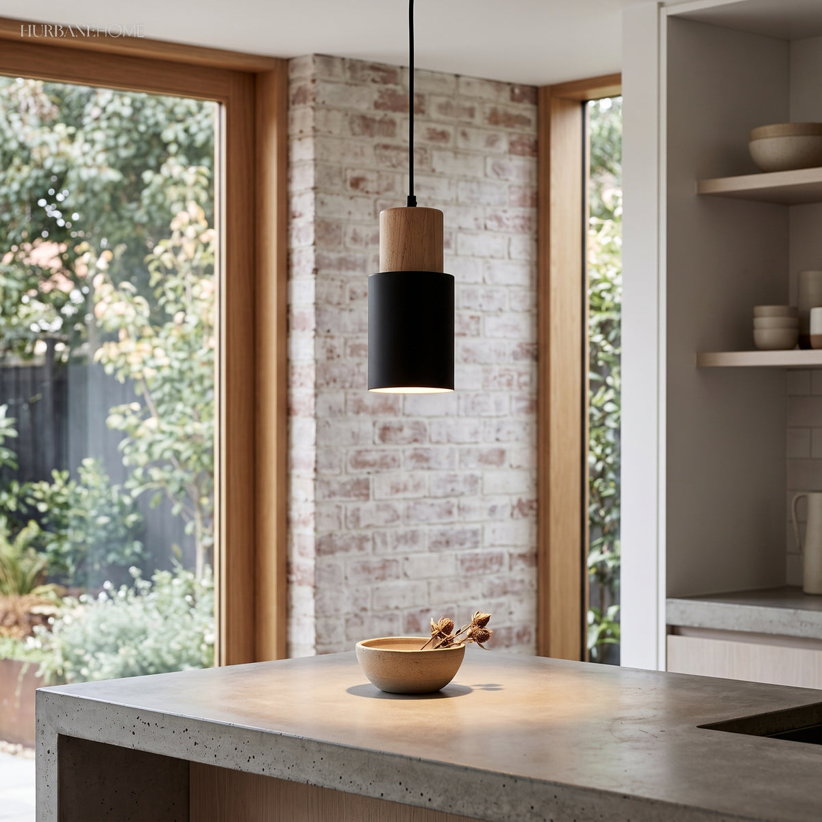 Black cylinder pendant lighting a concrete island against exposed brick