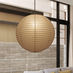 Round globe paper lantern lit in front of a pale brick wall