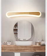 Curved wood vanity light lit above a round mirror and timber top