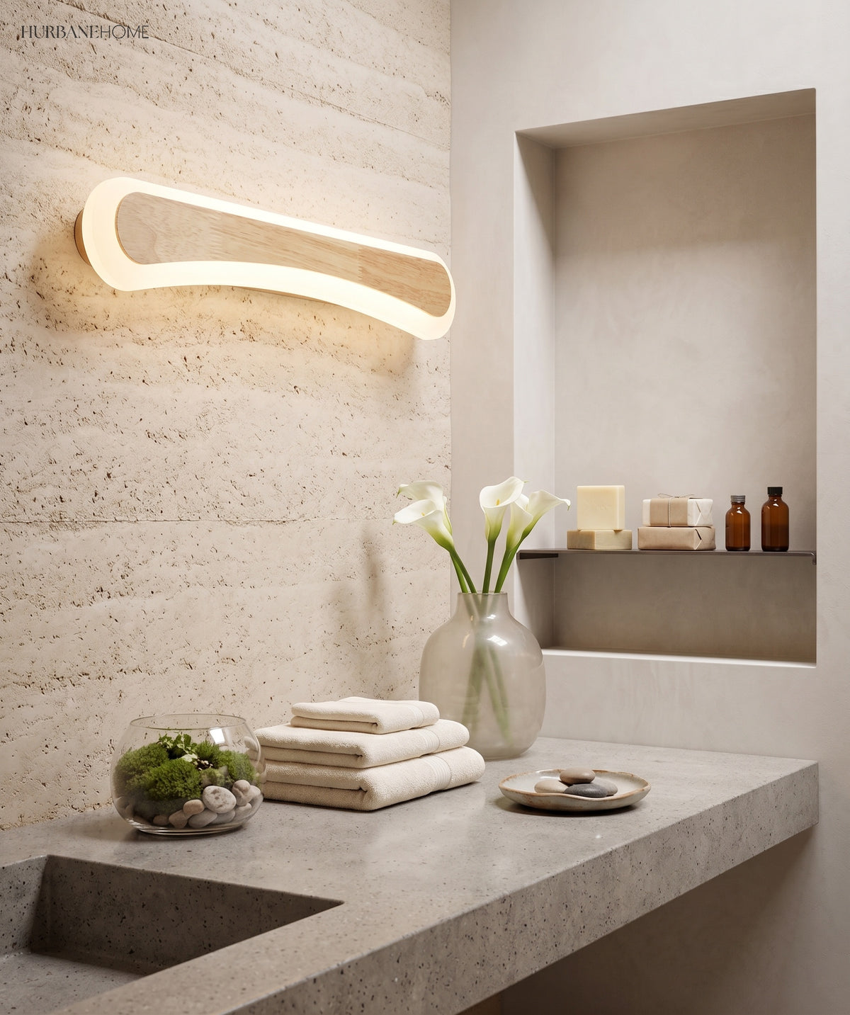 Curved wood vanity light lit in a stone niche above folded towels