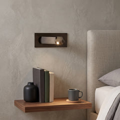 Bronze bedside reading wall sconce above a timber shelf and bed