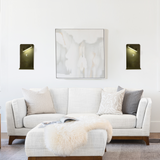 Two wall lamps flanking wall art with directional beams over a sofa