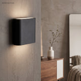 Black aluminum sconce beside a round mirror in a narrow hallway