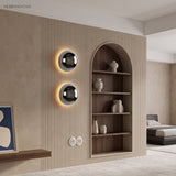 Two mirrored dome sconces lit on a pale wall beside an arched shelf