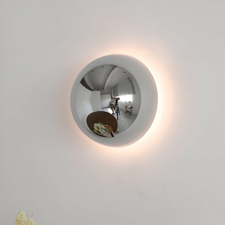 Silver mirrored dome sconce lit on a pale wall with a halo glow